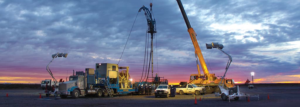 Sunset scene of onshore drilling with trucks, a crane and workers