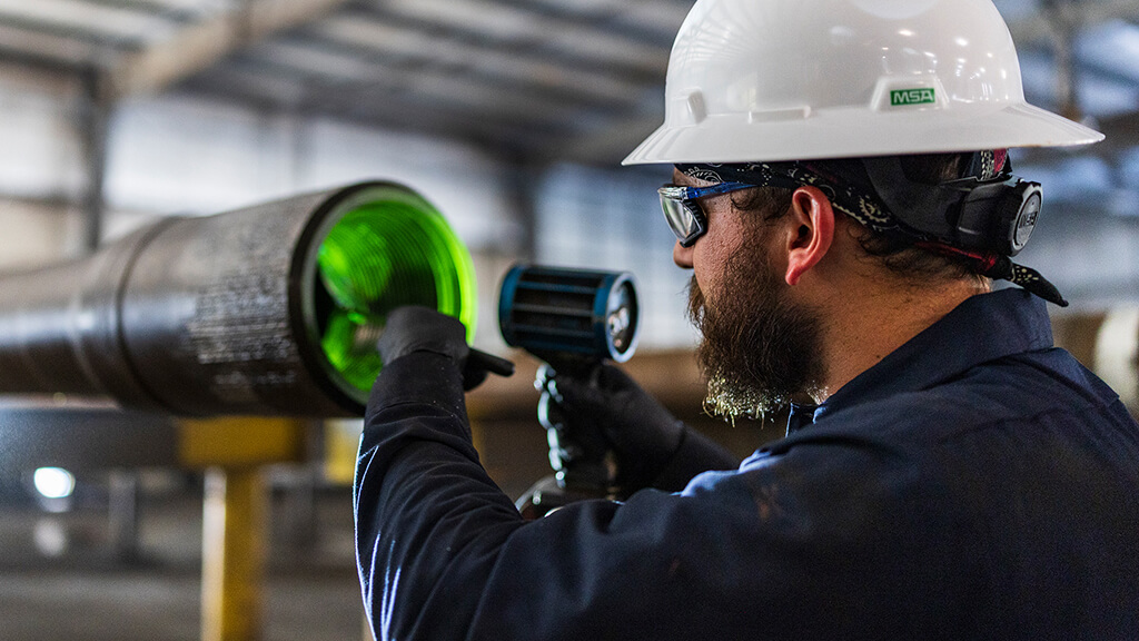 A Workstrings engineer inspecting a drill pipe with a green light